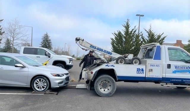 Ein weißer Abschleppwagen bereitet das Abschleppen eines silbernen PKW auf einem Parkplatz vor.